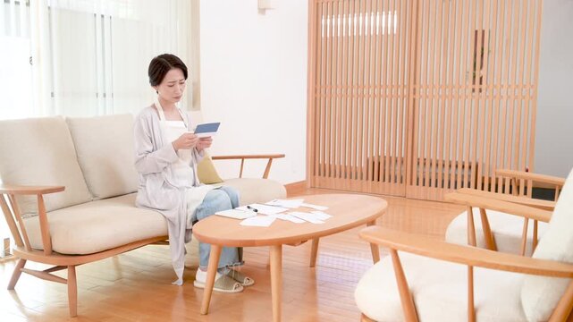 Japanese women struggling with high prices, rising utility bills, and the growing burden on household budgets; a wide-angle full-body video of a housewife looking at her bank statement in distress