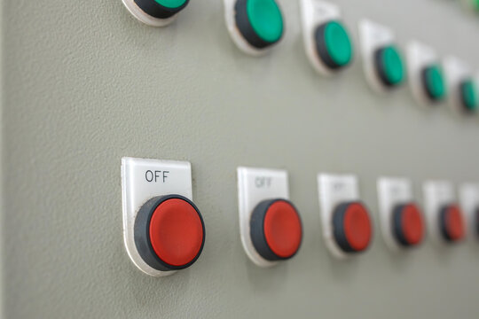 Row of red stop push buttons lines industrial equipment panel. Switchboard offers vital machinery control options with labeled off buttons beneath green indicator activation switches.