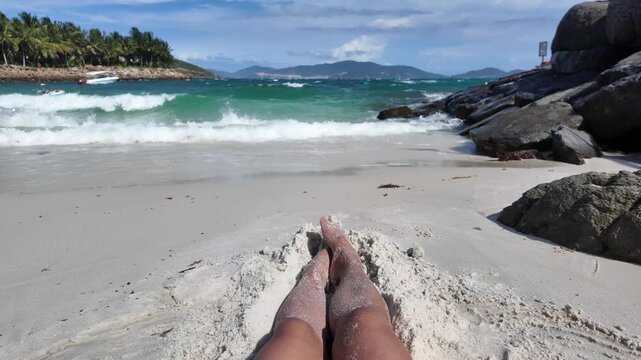 First-person POV beach vacation view of a woman lying down with sandy legs relaxing on a white sand tropical beach, watching turquoise waves roll ashore in Nha Trang, Vietnam