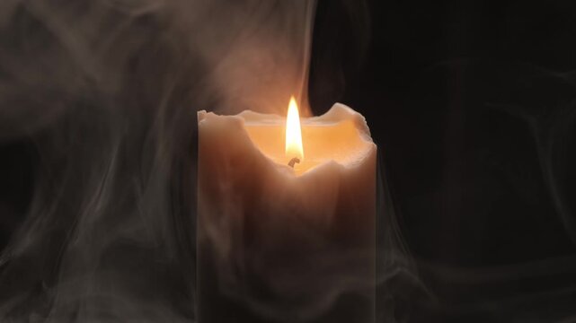 A thick cream-colored candle with an irregular, melted rim, burning with a bright flame and surrounded by thick smoke, rotates against a black background.