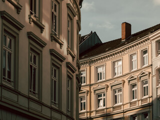 Low-angle view of classic European neoclassical building facades with ornate windows, decorative moldings, and terracotta tile roof bathed in warm sunlight against a soft blue sky. © nekko soup