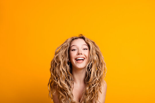Smiling young woman portrait with curly blonde hair against vibrant yellow background expressing joy and confidence in a bright studio headshot