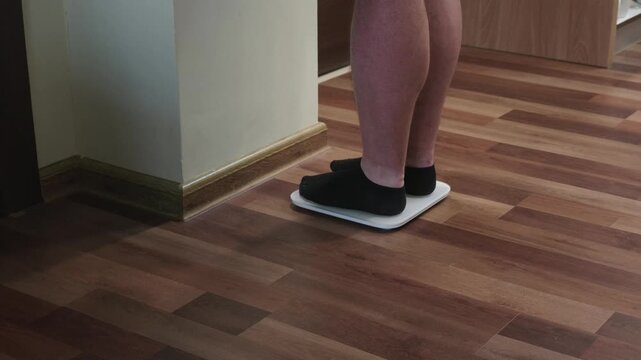 Domestic setting, a man wearing black socks prepares to step onto a sleek white digital scale to monitor his body weight