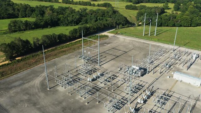 Electrical substation surrounded by rural fields and trees with power equipment, aerial establishing overview