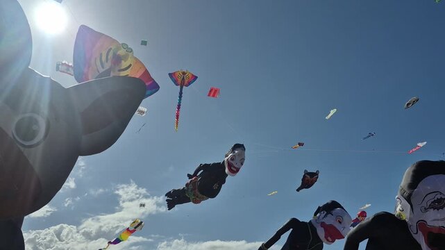 Large traditional kites flying above visitors during a colorful beach festival