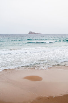 Ocean waves on a sandy beach with distant rocky island in a beach