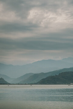 Calm lake with boats and mountainous landscape under cloudy sky