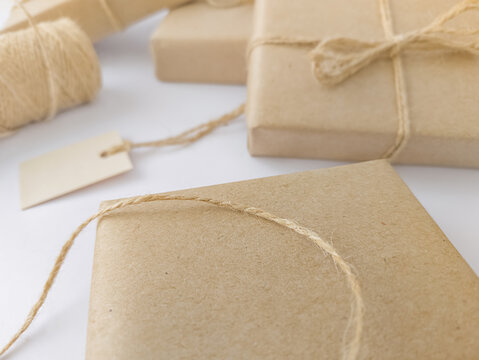 Close-up shot of gift boxes wrapped in craft paper with natural twine and blank tag on white background, concept of eco friendly packing and zero waste holiday celebration