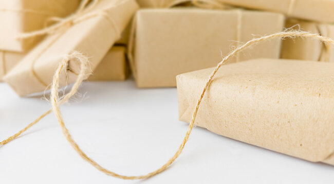 Close-up of gift boxes wrapped in brown craft paper with curved twine on a white background, concept of eco friendly holiday packaging and zero waste preparation