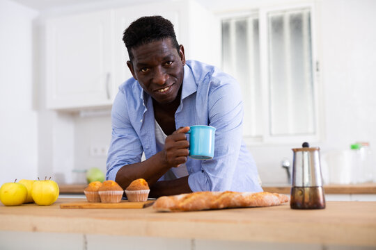 Smiling man enjoying his hot coffee in kitchen in apartment