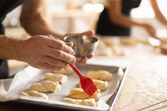 Baker's hands grease pieces of dough on baking sheet