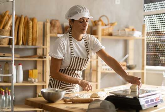 Elderly woman baker weighs pieces of dough