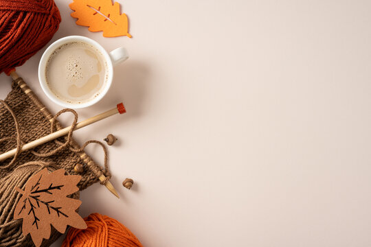 Cozy autumn knitting scene with yarn, needle, acorn and a warm cup of coffee on soft beige neutral table