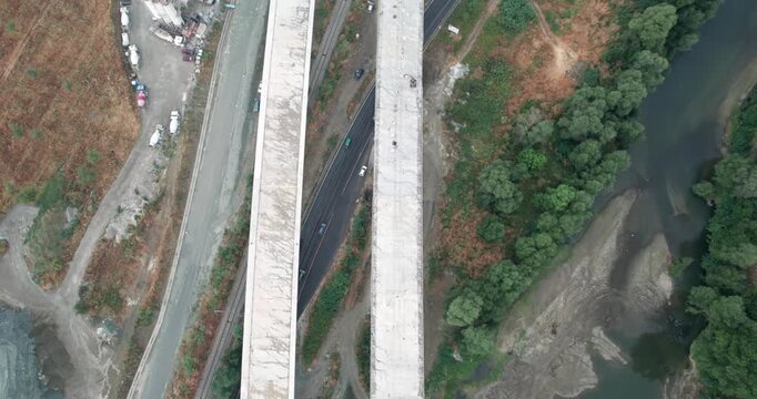 Highway construction site with bridge is shown in the air with a road and traffic below it, aerial view