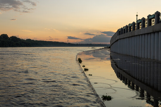 The river and embankment partially flooded with water along a high fence at sunset and twilight in Ufa, Bashkiria.