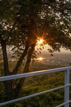 Warm sunset sun through tree and white railing overlooking private houses and industrial part of Ufa city, Bashkiria.
