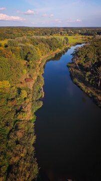 Vertical 9:16 top down aerial shot of a winding river and trees at golden sunset