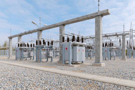 Large transformer units stand under a clear blue sky. Concrete pillars support heavy-duty electrical equipment. Metal frames hold insulators and wires, ready for power transmission