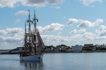 Fototapeta premium majestic vintage three masted wooden tall ship navigating through calm water near the coast on a sunny day with fluffy white clouds in the sky.