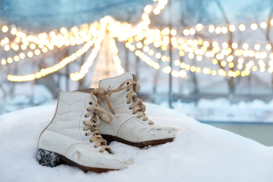 pair of white old figure skating skates close up in snow, at ice rink, abstract light nature background. Ice skating outdoor activities in winter season. soft focus