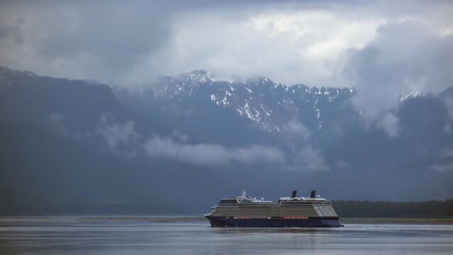 Luxury cruiseship cruise ship liner Solstice sailing the Inside Passage with panoramic mountain range glacier views in Fjord during Alaska Adventure Wilderness cruising with coast line and low clouds