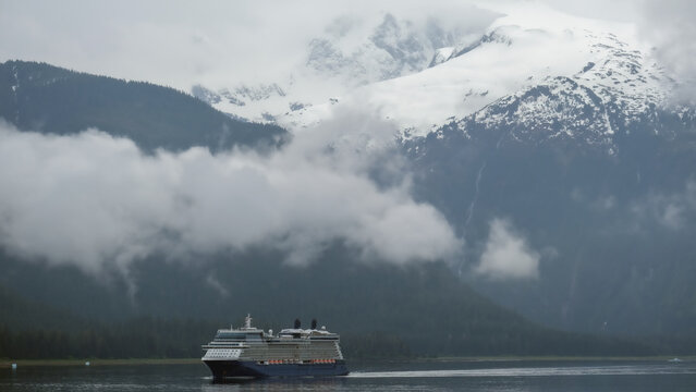 Luxury cruiseship cruise ship liner Solstice sailing the Inside Passage with panoramic mountain range glacier views in Fjord during Alaska Adventure Wilderness cruising with coast line and low clouds