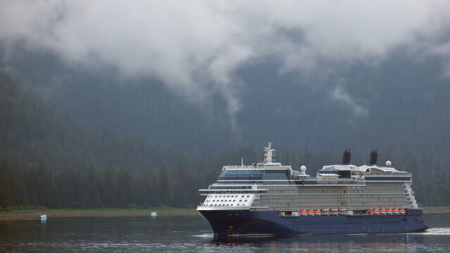 Luxury cruiseship cruise ship liner Solstice sailing the Inside Passage with panoramic mountain range glacier views in Fjord during Alaska Adventure Wilderness cruising with coast line and low clouds