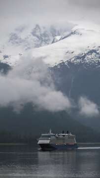 Luxury cruiseship cruise ship liner Solstice sailing the Inside Passage with panoramic mountain range glacier views in Fjord during Alaska Adventure Wilderness cruising with coast line and low clouds