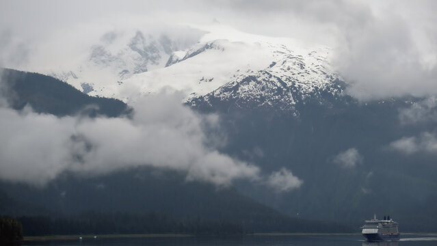 Luxury cruiseship cruise ship liner Solstice sailing the Inside Passage with panoramic mountain range glacier views in Fjord during Alaska Adventure Wilderness cruising with coast line and low clouds