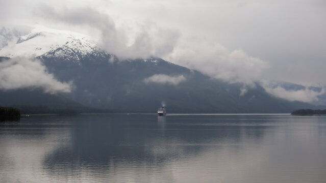 Luxury cruiseship cruise ship liner Solstice sailing the Inside Passage with panoramic mountain range glacier views in Fjord during Alaska Adventure Wilderness cruising with coast line and low clouds