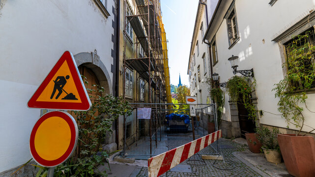 Narrow historic urban street with building renovation, scaffolding, construction barriers and warning signs, illustrating restoration work in a European city