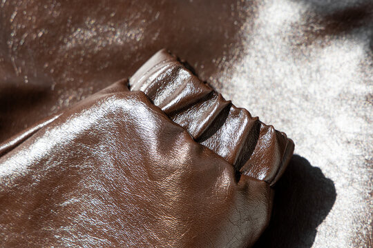 Brown leather sleeve cuff with elastic detail resting on a smooth dark brown leather background