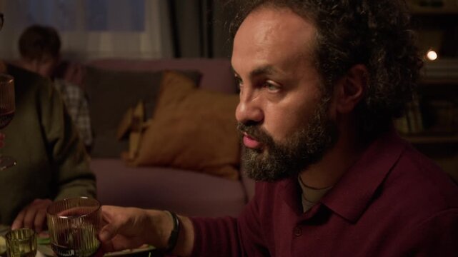 Middle aged Caucasian man drinking red wine and conversing during family dinner. Visual suitable for holiday campaigns, wine advertising, and festive lifestyle storytelling
