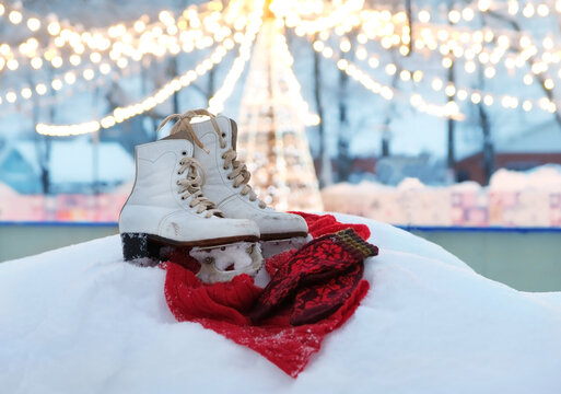 pair of white old figure skating skates, scarf and mittens in snow close up, at ice rink, abstract light nature background. Ice skating outdoor activities in winter season. soft focus