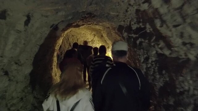 A group of people are walking through a tunnel visiting the Devil throat cave in Bulgaria. The tunnel is dark and the people are wearing backpacks