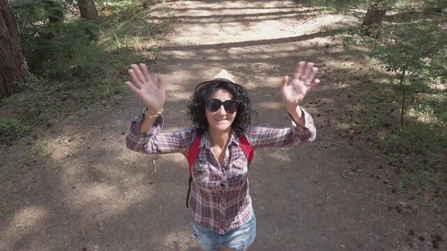 A woman wearing a hat and sunglasses walks down a dirt path. She is wearing a plaid shirt and shorts, aerial shot