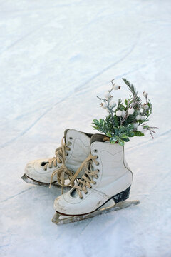 pair of vintage white figure skating skates with festive winter decor on snowy ice rink close up, abstract light nature background. Ice skating outdoor activities in winter season.