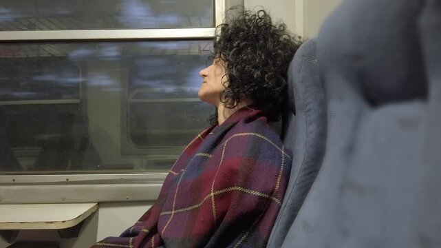 Sleepy traveler exhausted woman is sitting in a train with her head down and a blanket draped over her shoulders. She is relaxed and comfortable