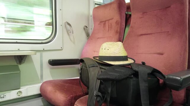 A hat and backpack are sitting on a red seat in a train. Concept of traveling, scene is casual and relaxed