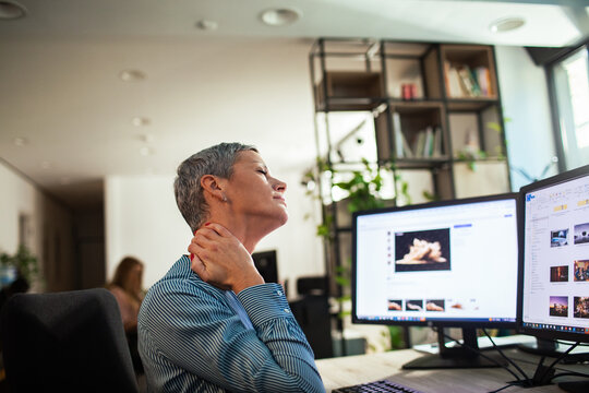Woman rubbing sore neck at office computer