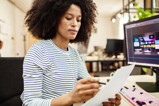 Woman reviewing printouts while designing ui at office desk