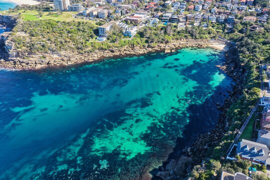Aerial view of Gordons Bay featuring turquoise waters, rocky coastline, and residential houses in Coogee, New South Wales, Australia.