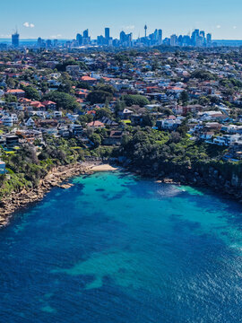 Aerial view of Gordons Bay with turquoise waters and rocky coastline, surrounded by houses in Coogee, with the Sydney skyline in the distance, Coogee, New South Wales, Australia.