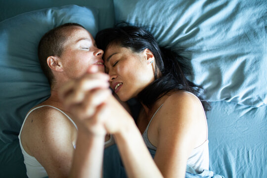 Two women holding hands while cuddling in bed