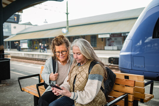 Two senior women checking a smartphone at a train station