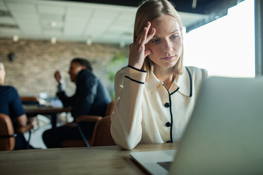 Stressed woman working on laptop in open office