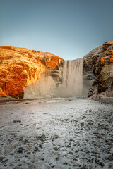 Skogafoss waterfall framed by snow and golden winter light in South Iceland view © CharnwoodPhoto