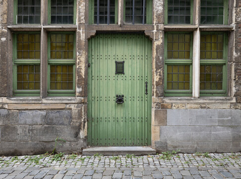 Ancient pale green door with metal studs and iron details in a stone wall in Ghent, Belgium, Europe