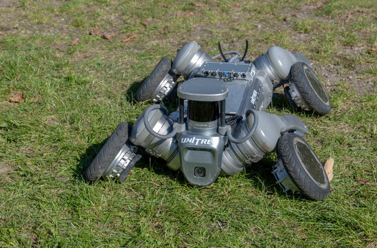 Unitree B2-W wheeled quadruped robot lying on grass, grey four-legged machine with rubber tires, RoboSense lidar sensor and antennas, outdoor robotics field test, side view, daylight