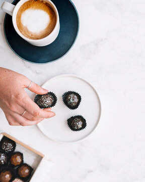 Chocolate bon bons being picked by hand near coffee cup